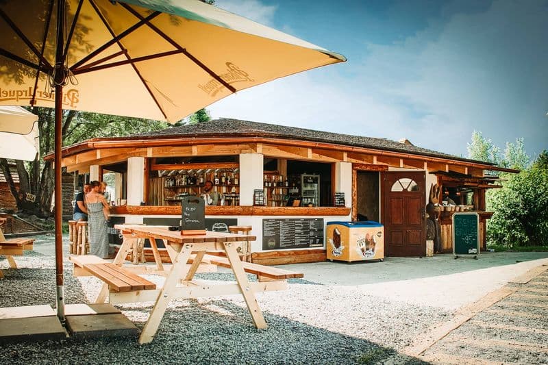 Letní bistro u minigolfu, před ním dřevěné stoly pod slunečníky
